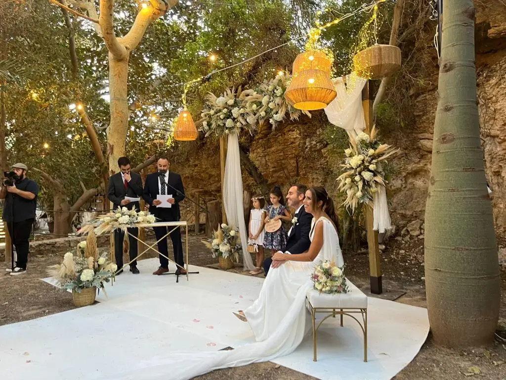 Una novia sentada bajo los árboles junto a la roca, con guirnaldas de luz, en su ceremonia
